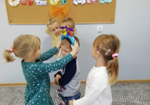 Dziewczynka zakłada chłopcu na głowę dmuchaną czapkę ze śmigłem.