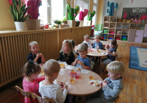 Dzieci siedza przy stolikach i częstują się łakociami.