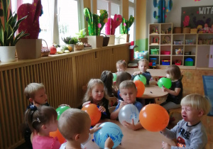 Dzieci siedza przy stolikach i maluja mazakami na kolorowych balonikach.