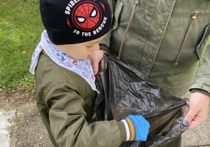 Chłopiec wyrzuca znalezione śmieci do plastikowego worka.