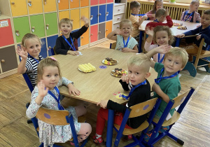 Dzieci siedzą przy stolikach, na których znajduje się słodki poczęstunek.