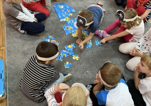 Dzieci siedzą na dywanie i układają puzzle przedstawiające mapę świata.