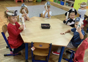 Dzieci siedzą przy stoliku i pozują do zdjęcia z własnoręcznie przygotowaną mapą skarbów.
