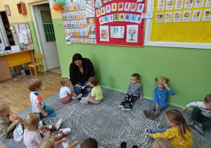 Grupa dzieci siedzi w kółku i patrzy na mamę, która czyta baśń.