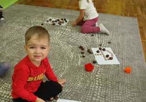 Dzieci układają jesienne szablony z kasztanami.