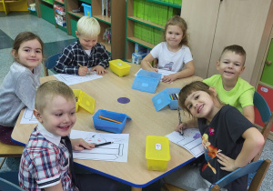 Pięcioro dzieci siedzi przy stoliku i maluje opaskę Superbohatera