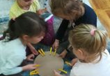 Dziewczynki na dywanie przyczepiają żółte spinki do koła.