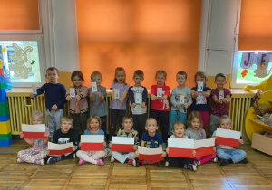 Dzieci z grupy Żabki trzymają napis BohaterOn oraz flagi Polski