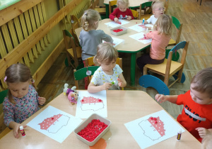 Dzieci z grupy Krasnale siedzą przy stolikach i wyklejają kontur Polski