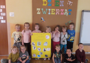 Grupa dzieci z plakatem przedstawiającym zwierzęta wykonanym na zółtym kartonie.