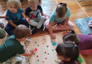 Dzieci przyklejają plastelinę na liściu, tworząc kropki.