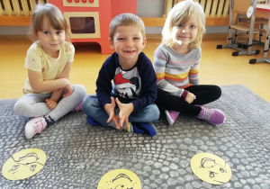 Przedszkolaki siedzą do okoła uśmiechniętej buzi ułożonej z klocków.