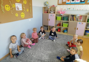 Dzieci siedzą na dywanie i uśmiechają się.
