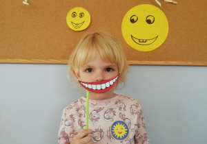Dziewczynka trzyma w ręku uśmiechnięte papierowe usta.
