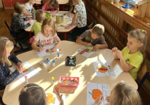 Dzieci przy stolikach wykonują jesienne opaski.