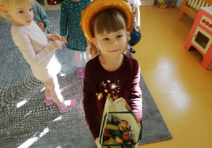 Dziewczynka z koroną na głowie trzyma w ręku papierową torebeczkę z cukierkami.