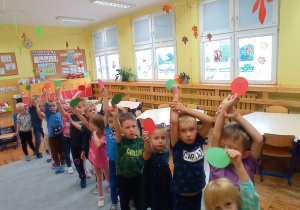 Piętnaścioro dzieci stoi na dywanie. Każde dziecko ma w dłoni koło: czerwone lub zielone. Dzieci ustawiły się w taki sposób aby powstał powtarzalny rytm: czerwone koło, zielone koło itd.