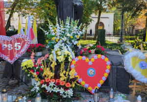 Pomnik Jana Pawła II przyozdobiony kolorowymi kwiatami, serduszkami, zniczami.