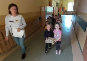 Stokrotki wraz z wychowawczynią maszerują w parach korytarzem przedszkolnym do kuchni aby upiec chleb.