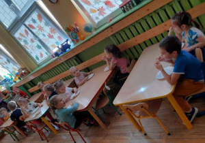 Dzieci z grupy Stokrotki przy stolikach zajadają upieczony chleb.