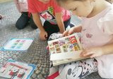 Dziewczynka i chłopiec z grupy „Liski” siedzą na dywanie. Dziewczynka w ręku trzyma klaser ze znaczkami pocztowymi.