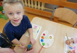 Dziewczynka z grupy „Liski” siedzi przy stoliku, w ręku trzyma pędzel zamoczony w farbie, maluje nim ziemniaka, którym wykona stempelek na pracy plastycznej.