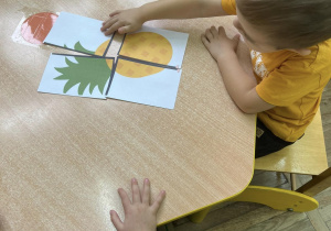 Dzieci przy stoliczku układają puzzle przedstawiające ananasa.