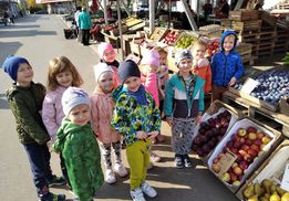 Grupa Motylki uśmiecha się stojąc przed straganem z warzywami i owocami na targowisku miejskim w Bełchatowie.