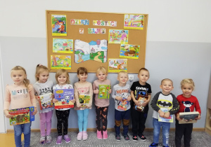 Dzieci trzymają książki i stoją na tle dekoracji z Dnia Postaci z Bajek.