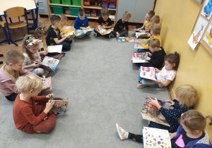 Dzieci siedzą w kole na dywanie i oglądają książeczki z bajkami.