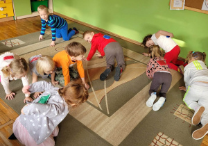 Grupa Misie na dywanie podczas kolejnej zabawy ruchowej. Dzieci spacerują na czworaka z woreczkami na plecach.