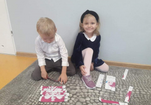 Dziewczynka i chłopiec układają puzzle z symbolami narodowymi.