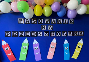 Zdjęcie przedstawiające dekorację z pasowania na przedszkolaka, na której widnieje napis, balony oraz kolorowe kredki.