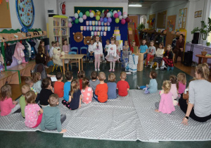 Dzieci z grupy Smerfy wystawiają przedstawienie dla najmłodszych grup z naszego przedszkola. Maluchy siedzą na kocach podziwiając występ.