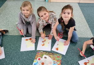 Trzy dziewczynki trzymają pędzle w dłoni i malują swoje misie.