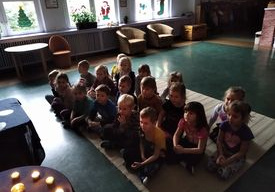 Dzieci z grupy Motylki siedza na dywanie i czekają na opowieści o wróżbach andrzejkowych. Przed nimi na stoliku łoną świeczki.