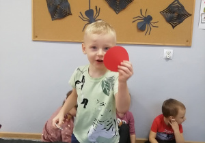 Chłopiec pokazuje czerwone koło trzymane w dłoniach.