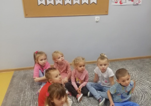 Dzieci siedzą na dywanie, a przed nimi lezą ilustracje związane z górnictwem.