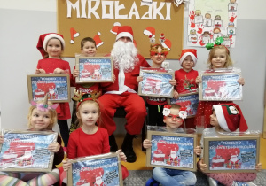 Dzieci siedzą i stoją dokoła Mikołaja w rękach trzymają prezenty.