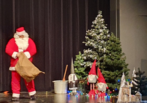 Zdjęcie przedstawiające Mikołaja na tle dekoracji świątecznej.