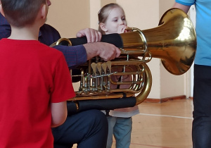 Wybrana przez muzyków dziewczynka próbuje zagrać na instrumencie, którym jest tuba.
