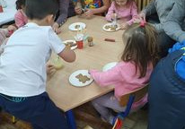 Dzieci siedzą przy stolikach mają przed sobą na talerzykach pierniczki, które dekorują. Obok siedzą rodzice.