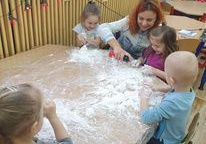 Dzieci siedzą przy stolikach przed sobą mają rozsypaną mąkę. Pni rozprowadza piankę do golenia.