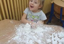 Dziewczynka w szarej bluzce z uśmiechem na twarzy miesza mąkę z pianką.