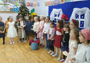 Zdjęcie grupowe przedstawiające dzieci stojące na tle dekoracji. Widoczna jest również choinka.