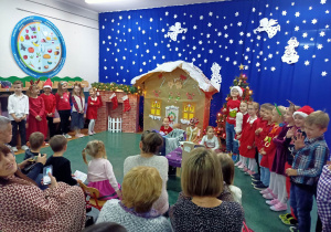 Dzieci w świątecznych strojach pozują na tle domku z piernika.
