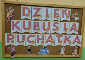 Tablica z napisem Dzień Kubusia Puchatka, wokół którego znajdują się emblematy przyjaciół Kubusia Puchatka