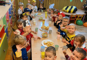 Zdjęcie grupowe dzieci, które siedzą przy stole, jedzą łakocie i machają.
