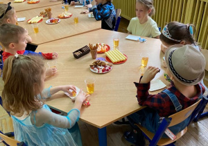 Dzieci z grupy Żabki siedzą przy stolikach i jedzą słodycze.