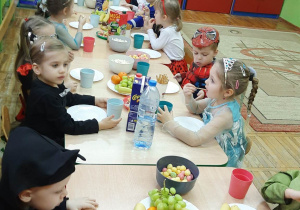 Dzieci z grupy Stokrotki siedzą przy stole w przebraniach i częstują się przygotowanym poczęstunkiem.